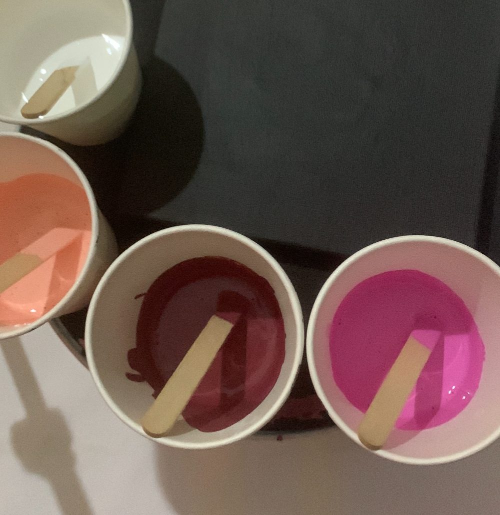 Mixing cups of red, pink and peach paint with stirring sticks on the studio bench